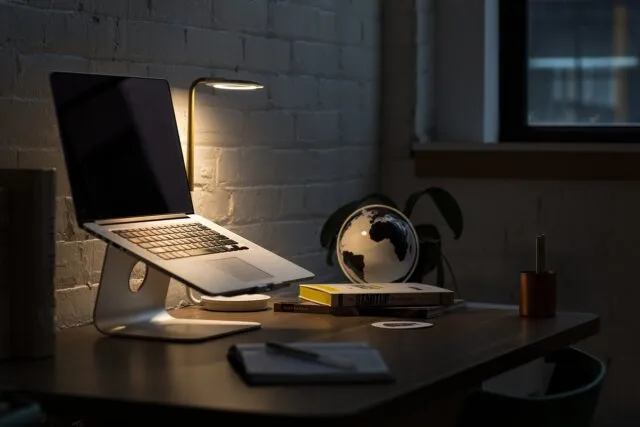Birou cu lampă aprinsă și laptop într-o după-amiază întunecată de toamnă
